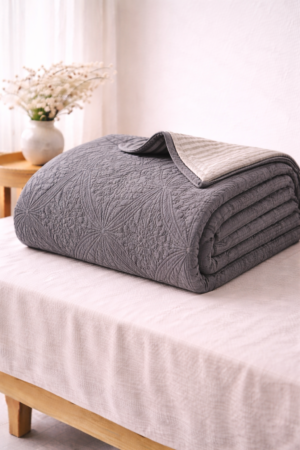 Charcoal grey cotton quilt with textured medallion stitching and striped underside in portrait style